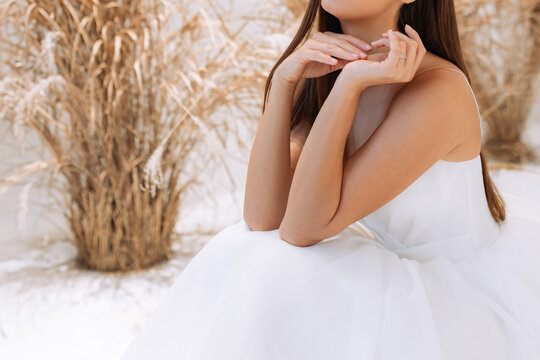 The hands of an elegant girl are folded near the chin on a white background in a dress.