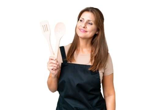 Middle age caucasian woman holding a rolling pin over isolated background looking to the side and smiling