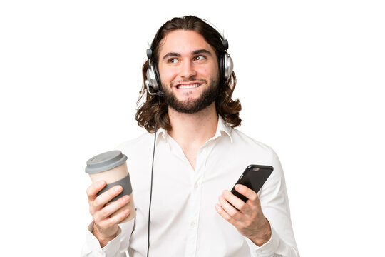 Telemarketer man working with a headset over isolated chroma key background holding coffee to take away and a mobile while thinking something