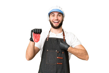 Butcher man wearing an apron and serving fresh cut meat over isolated chroma key background with surprise facial expression