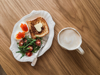 Delicious breakfast, brunch - toasts with butter, boiled eggs with red caviar, fresh salad and coffee on a wooden background, top view