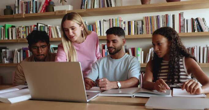 Young 20s European student girl showing to diverse schoolmates new assignment using laptop apps, explain university program, gain new knowledge using modern wireless tech. Teamwork, help and education