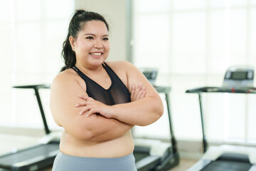 Overweight Asian woman exercise in gym, Cross arms, feeling relaxed and accomplished after workout, with treadmills behind. Content female in sportswear arm stretches, enjoying her fitness