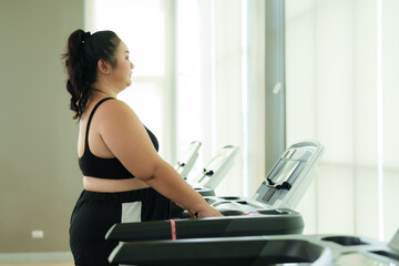 Fototapeta na wymiar Overweight Asian woman exercise in gym, determined woman at the gym prepares to begin her workout on a treadmill, embracing a healthy lifestyle. focused adult female stands on a treadmill,