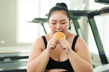 Chubby Asian woman exercise in gym, female savors snack, taking a moment to enjoy a treat during...