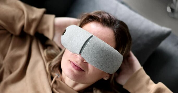 Tired woman puts massage glasses on eyes lying on couch. Multifunctional massagers for eyes and face