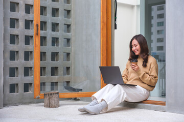 Portrait image of a young woman working on laptop computer and drinking coffee at home