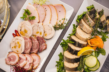 Close-up of two plates with assorted meat delicacies and slices of chopped stuffed fish with herbs .