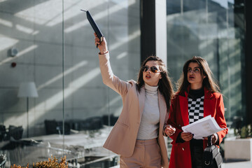 Two women in stylish business attire walking outdoors in urban setting.