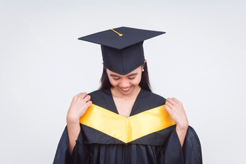 A cheerful young woman in a graduation cap and gown proudly adjusting her yellow stole, symbolizing academic success.