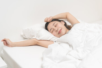 Fototapeta na wymiar Wake up, beautiful stretching asian young woman waking up after sleep comfortable, rest and relax, closed eyes while with covered blanket, girl stretch in her bedroom,in cozy white bed in the morning.