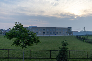 Obraz premium Modern school building - against a backdrop of a cloudy sky at dusk - surrounded by a well-maintained green lawn - bordered by a black fence. Taken in Toronto, Canada.