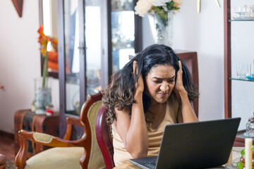 Unhinged, angry black-haired latin woman working on her laptop in her living room