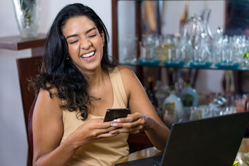 happy black haired latin woman chatting with her smartphone from her living room