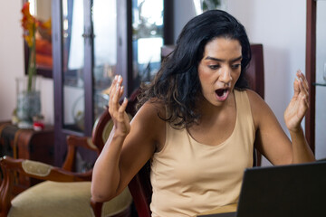 Unhinged, angry black-haired latin woman working on her laptop in her living room