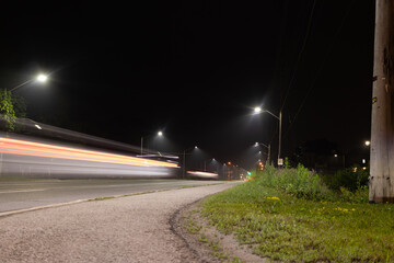 Nighttime cityscape - bright streetlights - red and white light trails streak across the road - passing vehicles long exposure. Taken in Toronto, Canada.