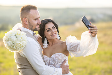 A young wedding couple is taking a selfie while enjoying a romantic moment in the park