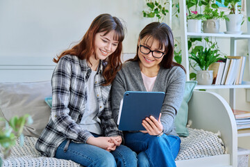 Happy mother and teenage daughter looking together at screen of digital tablet