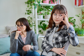 Conflict between mother and teen daughter, offended teenage girl sitting with back