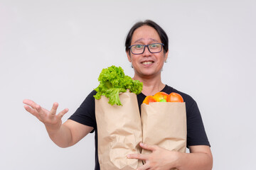 Cheerful man holding paper bags full of fresh vegetables and fruits, promoting a healthy lifestyle.