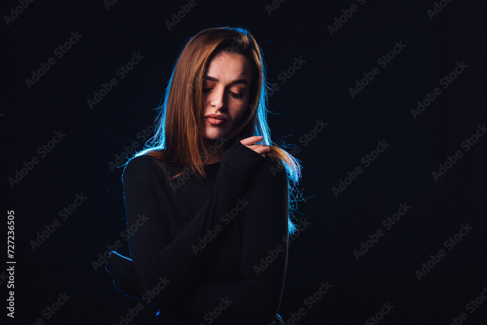 Wall mural Portrait of beautiful young woman in black sweater on black background