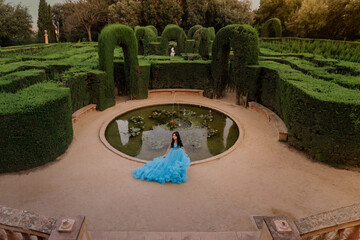 Portrait of a gorgeous young brunette girl in a blue evening ball dress with an open back standing on the steps of the palace staircase.