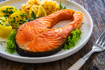 Fried salmon steak with boiled potatoes and sauerkraut on wooden table
