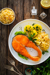 Fried salmon steak with boiled potatoes and sauerkraut on wooden table
