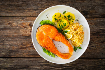 Fried salmon steak with boiled potatoes and sauerkraut on wooden table
