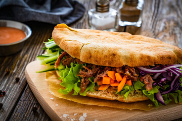 Pita - big sandwich with pulled beef and fresh vegetables on wooden table
