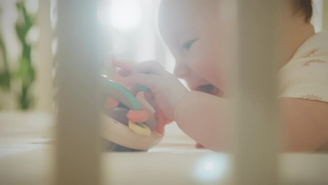 A small newborn child plays with a toy while exploring the modern world. A toy rattle in the hands of a small child. A newborn baby lies in a crib playing with a toy that improves hand motor skills