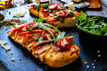 Focaccia - roasted mozzarella sandwiches with ham, tomatoes and arugula on black stone plate
