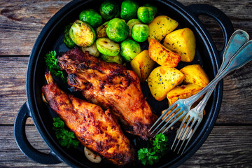 Cooked rabbit thighs with potatoes and brussels sprout in frying pan
