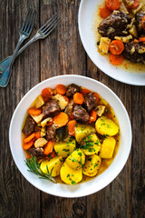 Roast pork cheeks with carrots and celeriac in sauce with boiled potatoes on wooden table 