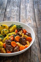 Roast pork cheeks with carrots and celeriac in sauce with boiled potatoes on wooden table 
