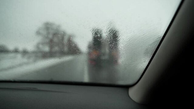 POV view from a car while driving in the rain on a snowy road. A car overtakes a large truck with a trailer. First-person view passenger traveling by car on a cloudy spring or winter day. Splashes