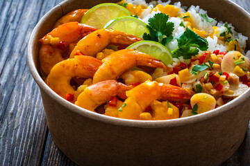Fried shrimps with rice and vegetable salad in lunch box to go on wooden table
