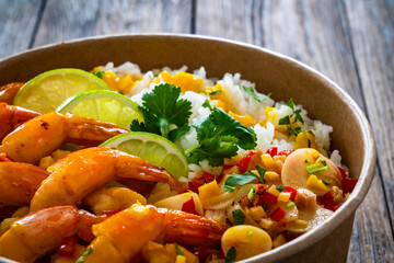 Fried shrimps with rice and vegetable salad in lunch box to go on wooden table
