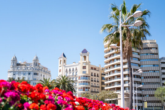 Valencia, Spain - May 12 2023 : famous Latin Mediterranean architecture, cuban style building in the middle with blue sunny sky, bright red flowers and palm trees. Great vacation photo