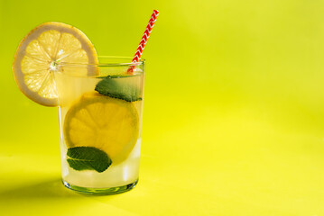 Glass of lemonade with lemon slices and mint inside, with a straw and ice, close-up, greenish background.
