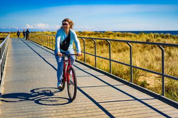 Mid adult woman riding bicycle at seaside
 - obrazy, fototapety, plakaty