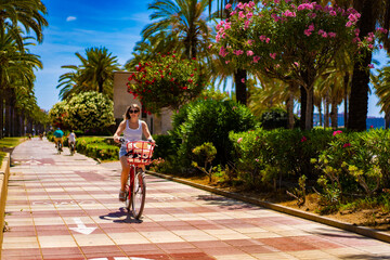 Fototapeta na wymiar Woman riding bicycle on seaside boulevard Costa Dorada Spain 