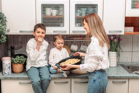 Mom and her children in the kitchen with pasta in the pan for dinner
