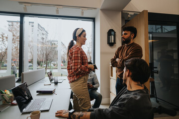 A group of colleagues engage in a casual conversation in a well-lit modern office environment, promoting teamwork and collaboration.