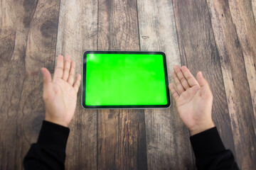 Mock up of a hand holding an iPad tablet with a greenscreen against a wooden texture background