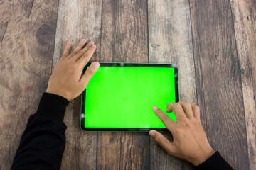 Mock up of a hand holding an iPad tablet with a greenscreen against a wooden texture background