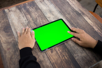 Mock up of a hand holding an iPad tablet with a greenscreen against a wooden texture background