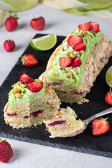 Meringue roll with strawberries and pistachios on slate board on gray background
