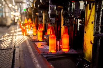 Glass factory, production of glass containers. Molten glass is blown into molds. Robotics in...