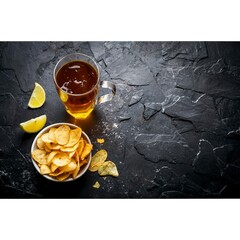 Beer with chips in a glass bowl. On black rustic background